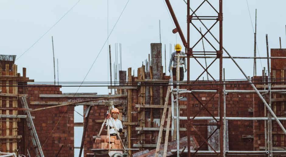Construction worker on scaffolding at a building site with brickwork and cranes